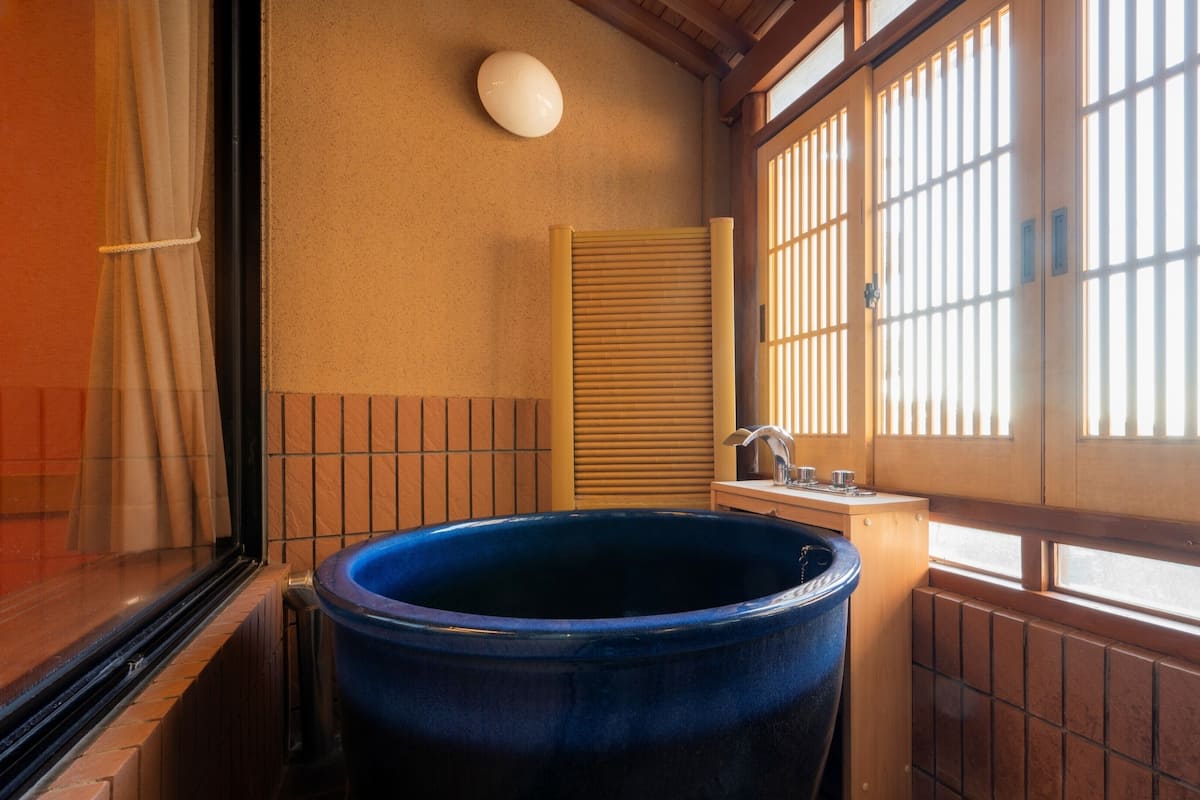 Um quarto em estilo japonês tradicional com tatames, um grande recipiente de cerâmica azul, um painel shoji de madeira e uma porta deslizante.