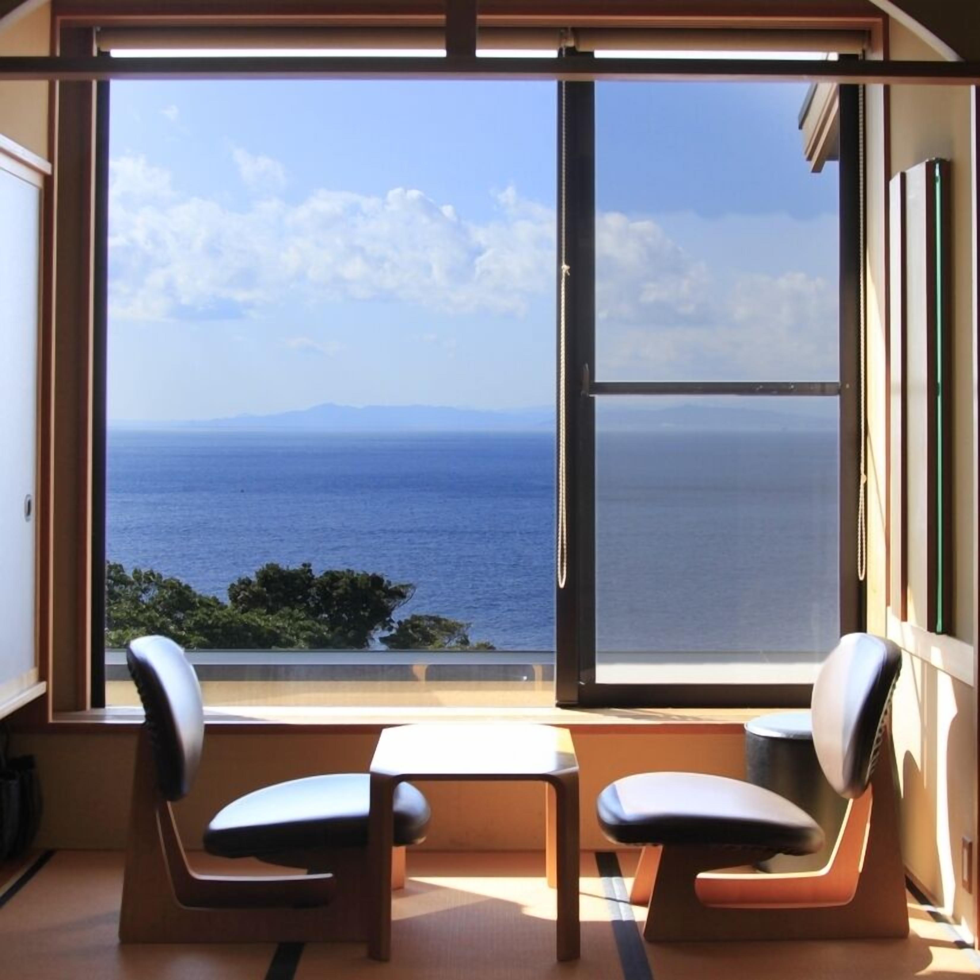 Una habitación con un gran ventanal con vista al mar, dos sillas y una pequeña mesa.