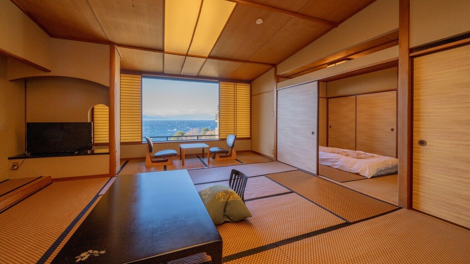 Una habitación japonesa tradicional con suelo de tatami, una mesa baja, sillas, una cama y un televisor.