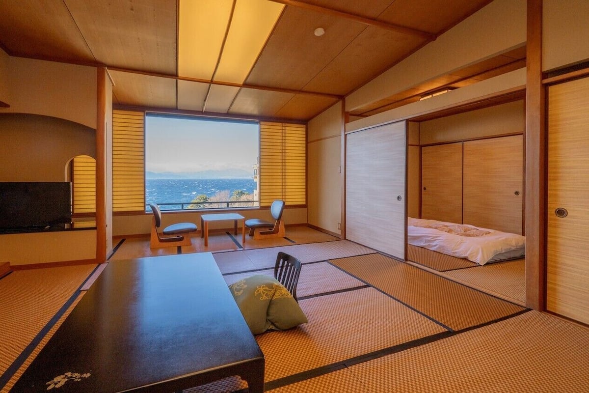 Una habitación japonesa tradicional con suelo de tatami, una mesa baja, sillas, una cama y un televisor.