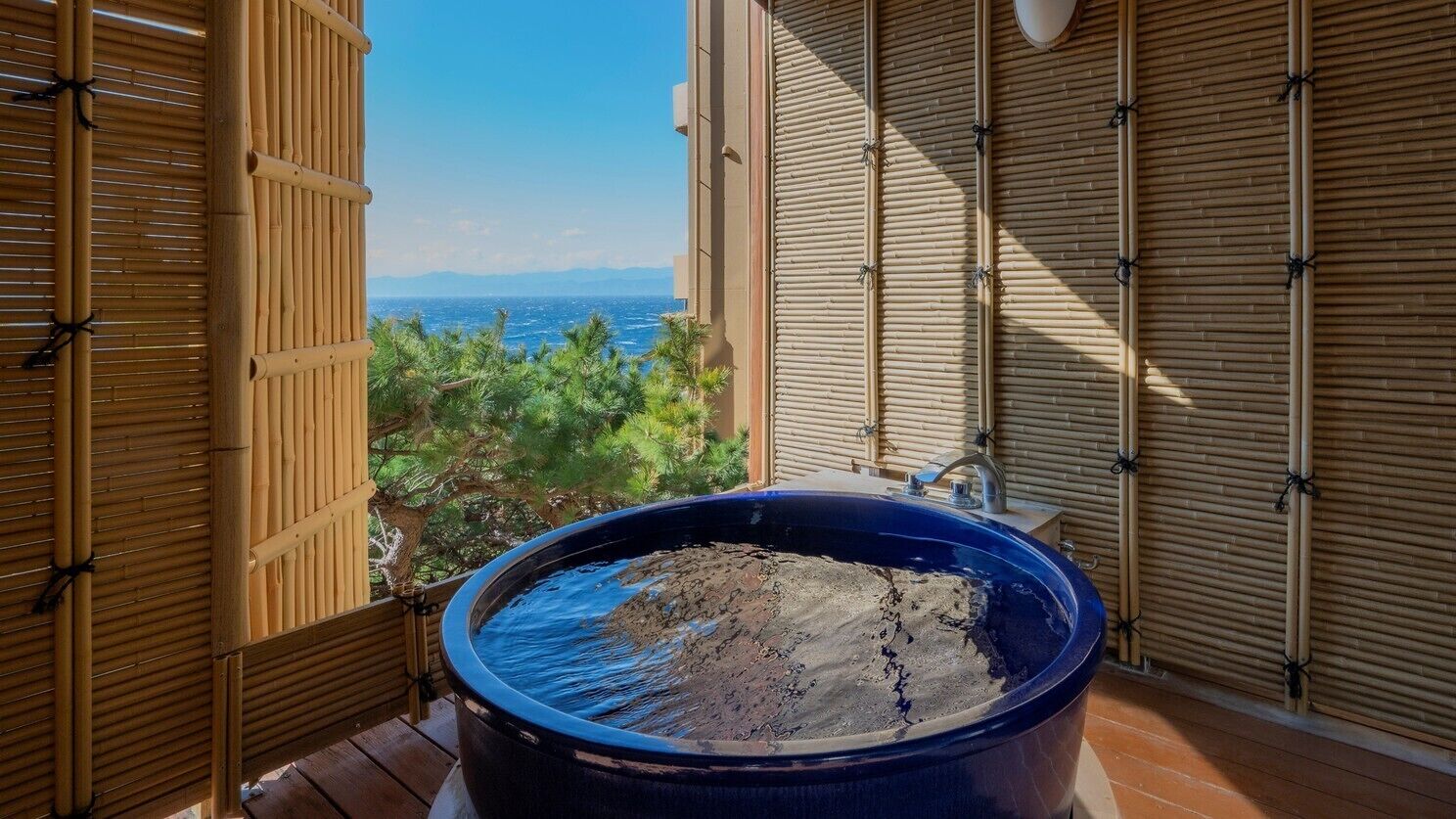 Una bañera azul grande sobre una cubierta de madera con vista al océano.