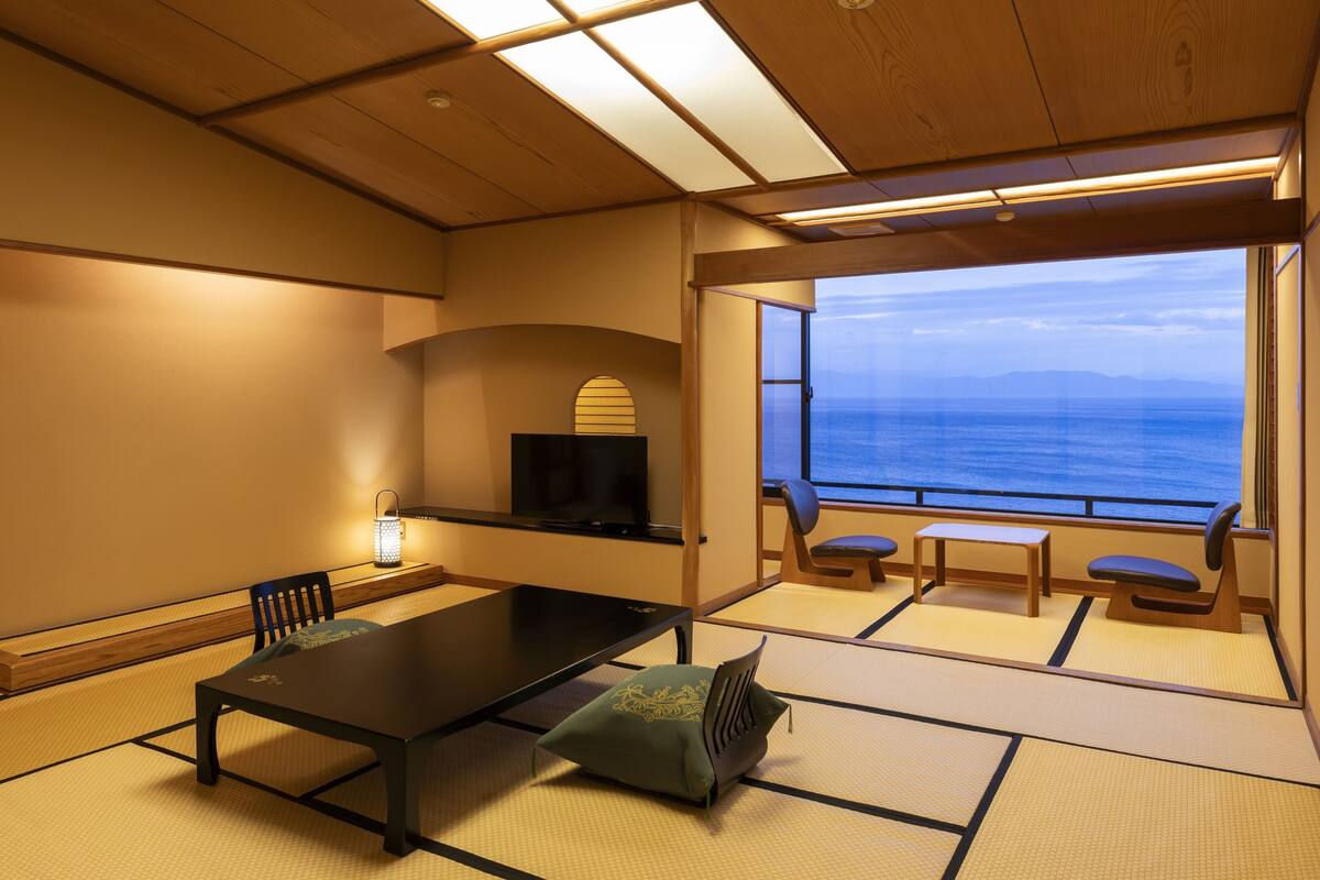 Quarto com tatame, uma mesa baixa, cadeiras, televisão e vista para o mar.