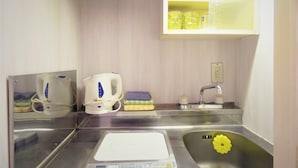 Une cuisine compacte équipée d’un évier en acier inoxydable, d’une bouilloire, d’une balance et d’une petite étagère où sont rangés des verres.