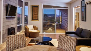A modern living room with a fireplace, a large window, and a view of the mountains. - Panoramia Villas (Myrtleford)