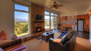 A spacious living room with a fireplace, large windows, and a view of the countryside. - Panoramia Villas (Myrtleford)