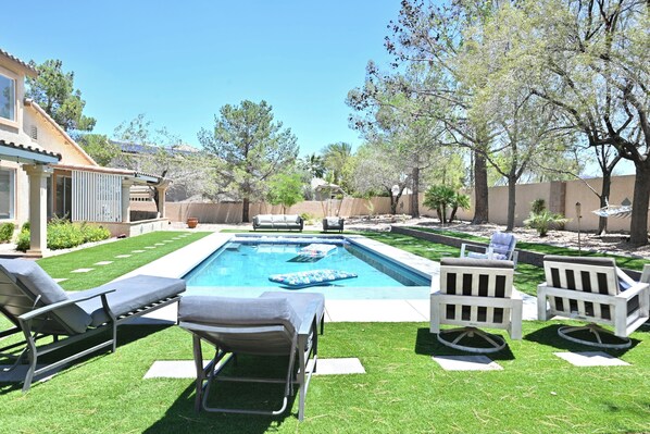 A backyard with a swimming pool, lounge chairs, and a patio area.