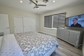 A bedroom with a bed, a television, a ceiling fan, and a window with blinds.