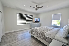 A bedroom with a bed, a ceiling fan, a TV, and a window with blinds.