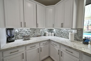 A kitchen with white cabinets, a marble countertop, a blender, a toaster, and a tiled backsplash.