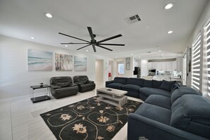 A modern living room with a sectional sofa, a ceiling fan, and artwork on the walls.