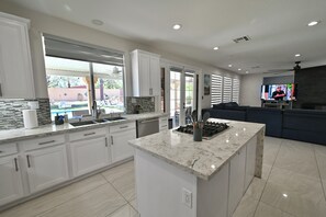 A modern kitchen with white cabinets, a marble island, and a built-in oven.