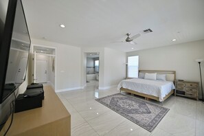 A bedroom with a bed, a TV, a ceiling fan, and a bathroom visible through an open door.