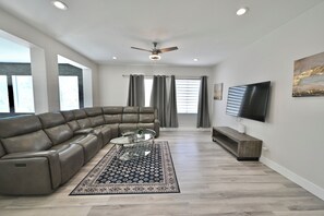 A modern living room with a sectional sofa, a glass coffee table, a wooden entertainment unit, and a mounted TV.
