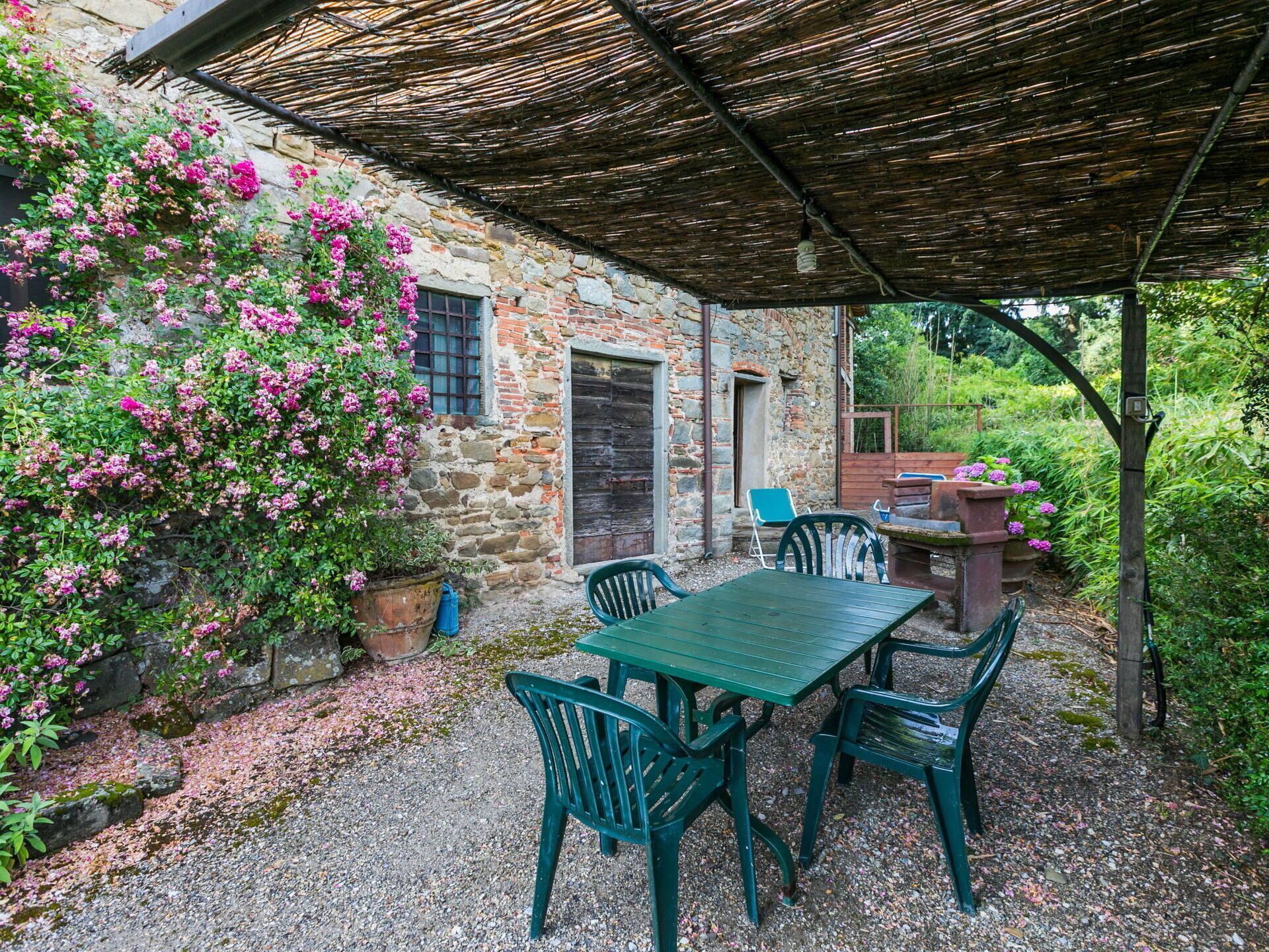 An outdoor patio with a table and chairs, a stone wall, and flowering plants.