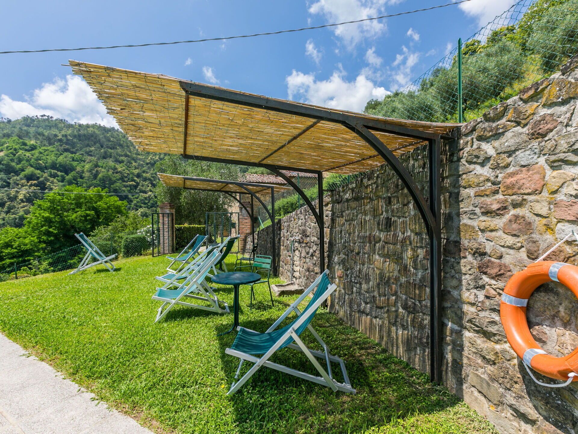 Un espace extérieur abrité, avec des chaises et des tables, un mur en pierre et une bouée de sauvetage.