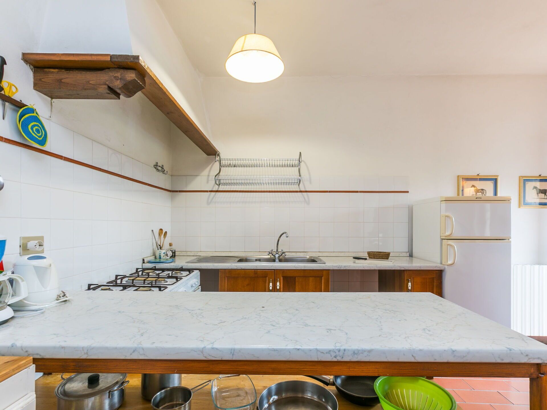 A kitchen with a marble countertop, wooden cabinets, a gas stove, and a hanging light fixture.