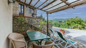 A covered patio with wicker furniture, a stone wall, and a view of the countryside. - Beautiful apartment for 4 guests with pool, WIFI, patio and pets allowed (Pescia)