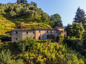 A stone building with a tiled roof, surrounded by lush greenery and trees.