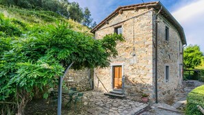 Un edificio de piedra con puerta de madera, una escalera de piedra y un jardín con mesa y sillas.