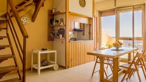 A spacious kitchen with wooden cabinets, a dining area with a table and chairs, a staircase, and a view of the sea through large windows. - La Plage - Home and Sea (Nizza Di Sicilia)