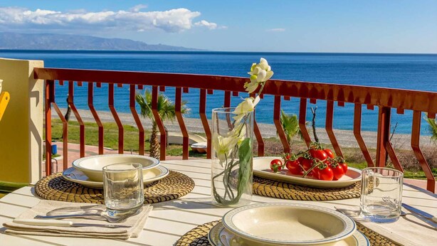 A table set for two with a view of the sea, a vase with flowers, and a plate of tomatoes. - La Plage - Home and Sea (Nizza Di Sicilia)