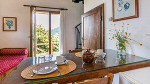 Zona pranzo con tavolo in vetro, divano rosso con motivo decorativo e vista su piante.