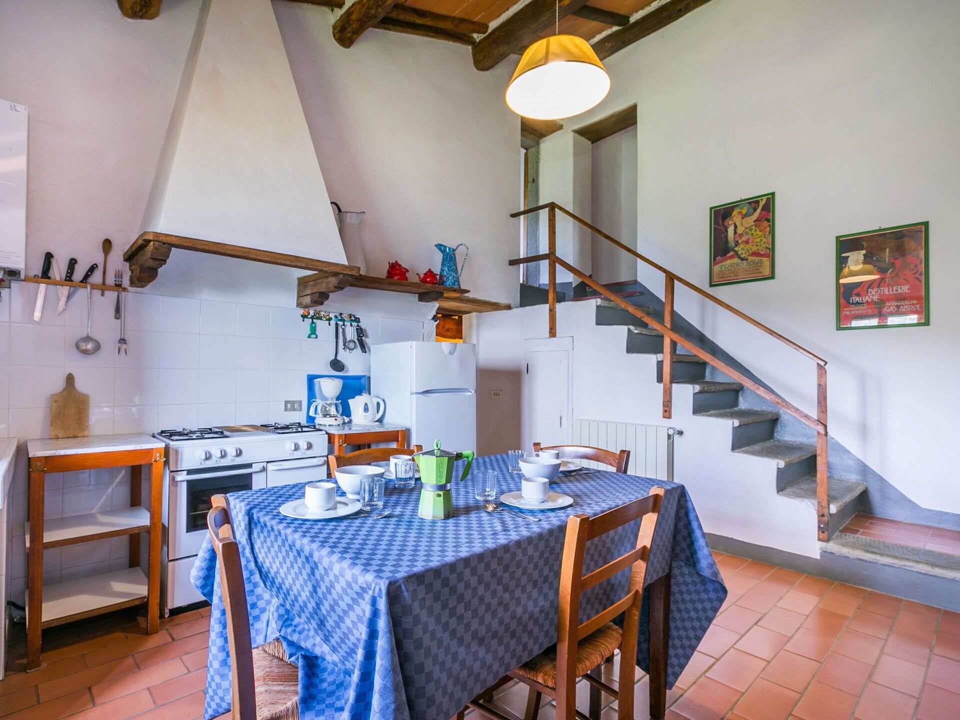 A rustic kitchen with a dining table set for two, a gas stove, and a wooden staircase.
