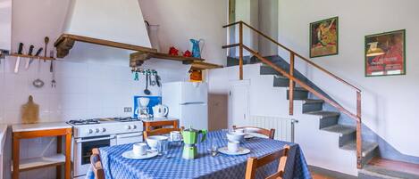 A rustic kitchen with a dining table set for two, a gas stove, and a wooden staircase.