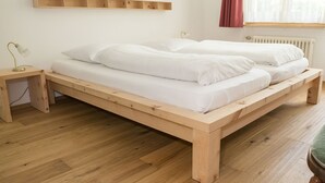 Ein Bett aus Holz mit weißer Bettwäsche in einem Zimmer mit Holzboden, einem Nachttisch und einem an der Wand befestigten Regal.