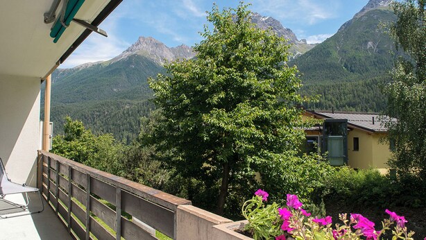 Ein Balkon mit Blick auf ein Gebirge, einem Holzzaun und ein Gebäude mit gelber Fassade.