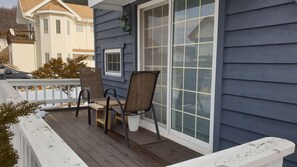 A covered porch with two chairs and a table, a sliding glass door, and a view of a neighboring house. - Under Hill Pension (Pyeongchang)
