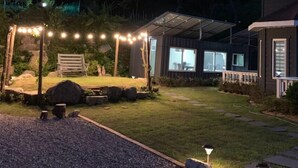 A house with a covered patio, a lawn, and a gravel path. - Under Hill Pension (Pyeongchang)