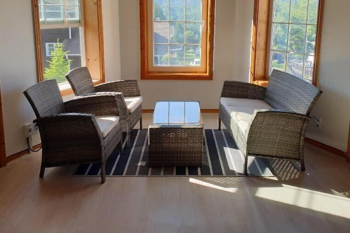A room with a corner sofa set, a coffee table, and large windows with blinds.