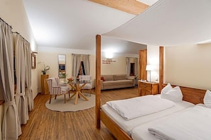 A hotel room with a four-poster bed, a sofa, a dining table with chairs, and a small kitchen area.