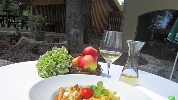 A dining table with a plate of pasta, a glass of white wine, and a bottle of water.