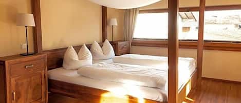 Una habitación con una cama con dosel, mesitas de noche de madera y un ventanal grande.