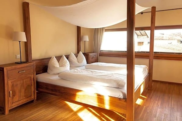 A room with a four-poster bed, wooden nightstands, and a large window.