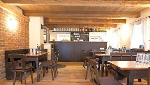 A restaurant with wooden tables and chairs, a brick wall, and a bar area with shelves of bottles.