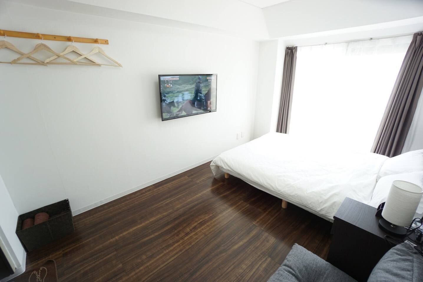 A modern hotel room with a wooden floor, a bed with white bedding, a mounted TV, and a window with curtains.