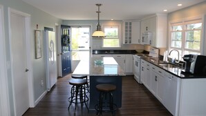 Una cocina moderna con armarios blancos, una isla grande con taburetes y una lámpara colgante.