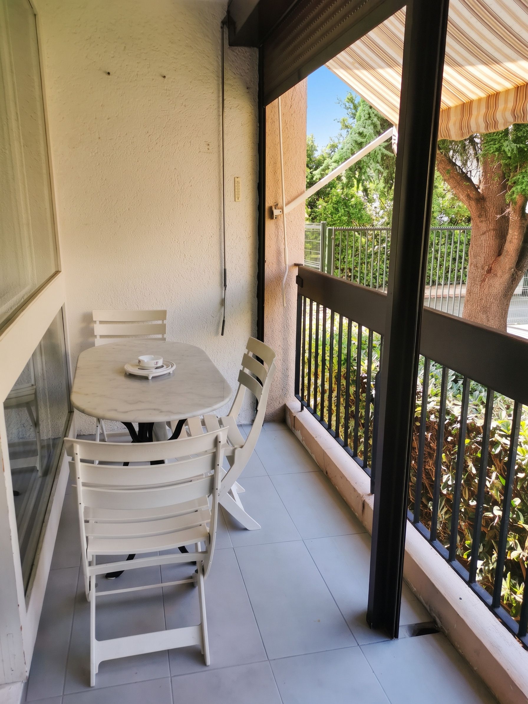 Un balcon avec une table et des chaises, une vue sur les arbres et une balustrade.