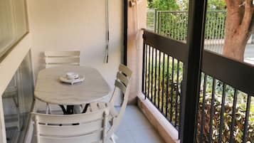 Un balcón con mesa y sillas, vistas a árboles y una barandilla.