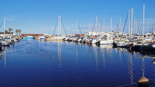 Un port de plaisance où sont amarrés de nombreux bateaux, l’eau est calme et le ciel est dégagé.
