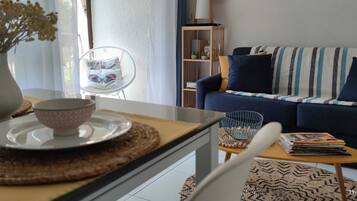 Ett vardagsrum med en soffa, ett soffbord, en fåtölj, en bokhylla och en vas med torkade blommor.