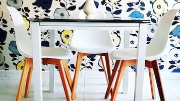 Een eettafel met vier stoelen, een vaas met gele bloemen en een behang met bloemenmotief.