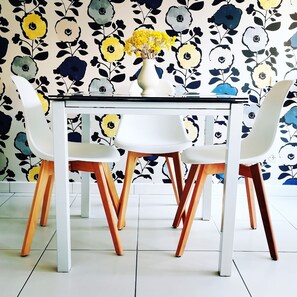 A dining table with four chairs, a vase with yellow flowers, and a floral wallpaper pattern.