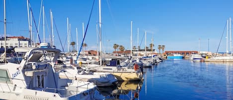 A marina with multiple boats docked, calm water, and a clear sky.
