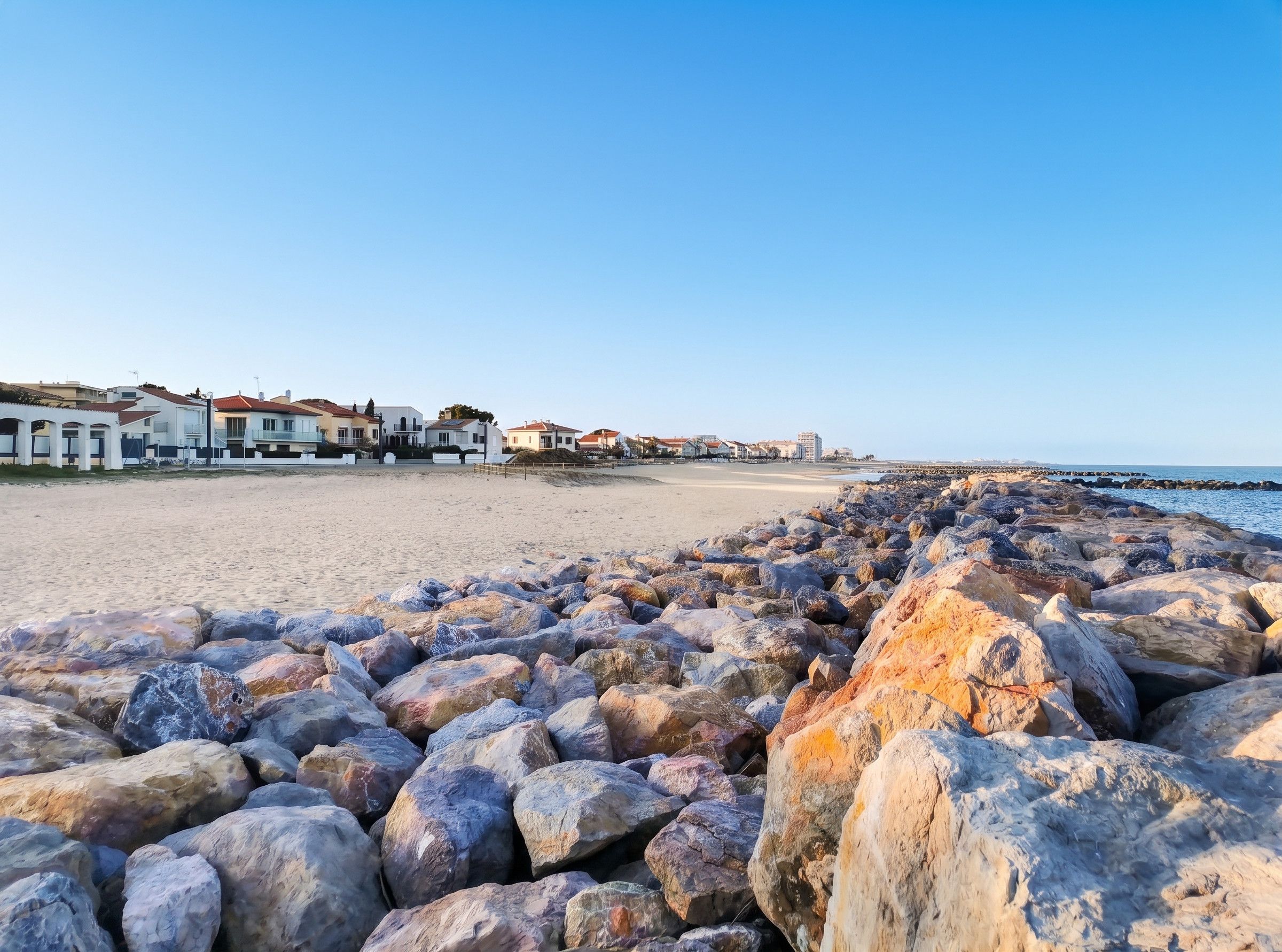 A beach with a rocky shoreline and buildings in the background.