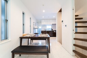 A modern kitchen with white cabinets and a dining area with a bench and table set for two. - Satellite Hotel Yebisu (Tokyo)