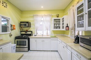 A kitchen with white cabinets, a stove, a microwave, and a coffee maker. - Amazing Beachfront Paradise - Chateau Monique (Lower Carlton)